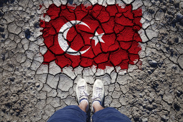 Top view of a Turkey resident standing on cracked soil with torn and cracked Turkey flag.