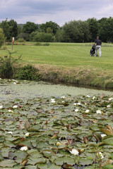 A golfer walking towards the green on a par 3 with water in the foreground