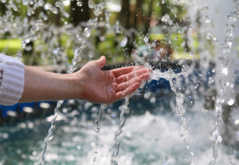 Hand touches clean and fresh water from the fountain.