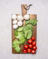 bunch of cherry tomatoes, spinach and mushrooms on a cutting board on wooden rustic background top view close up