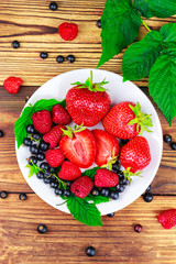 Mix of fresh, ripe berries in plate on wooden background.