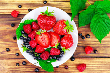 Mix of fresh, ripe berries in plate on wooden background.