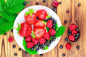 Mix of fresh, ripe berries in plate and spoon on wooden background, top view.