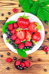 Mix of fresh, ripe berries in plate and spoon on wooden background, top view.