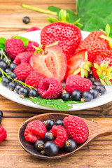 Mix of fresh, ripe berries in plate and spoon on wooden background.