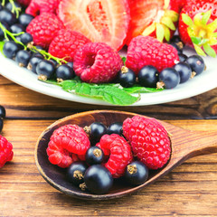 Mix of fresh, ripe berries in spoon and plate on wooden background, selective focus.