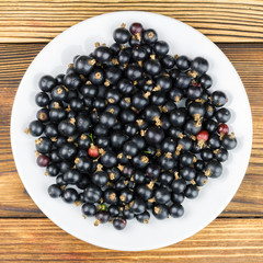 Black ripe currant in plate on wooden background, top view