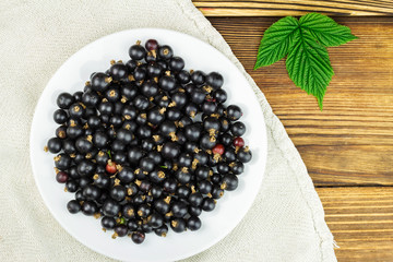 Black ripe currant in plate on old linen canvas, wooden table