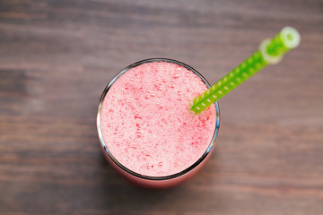 A watermelon smoothie in a glass with tube on a wooden background