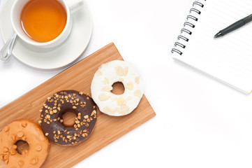 Delicious donuts with icing, book and tae in wood plate isolated on white