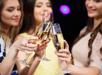 Clinking glasses of champagne in hands on bright lights backgrou