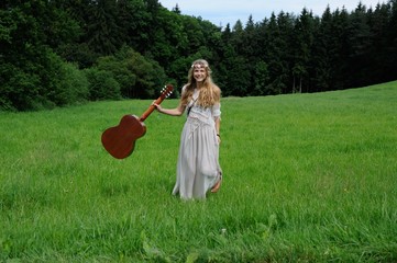 Junge Frau in Hippie-Kleidung mit Gitarre auf einer Wiese