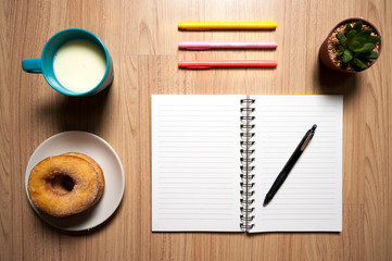 Office wood desk table with book,  supplies, donut and milk cup. Top view, Flat lay.