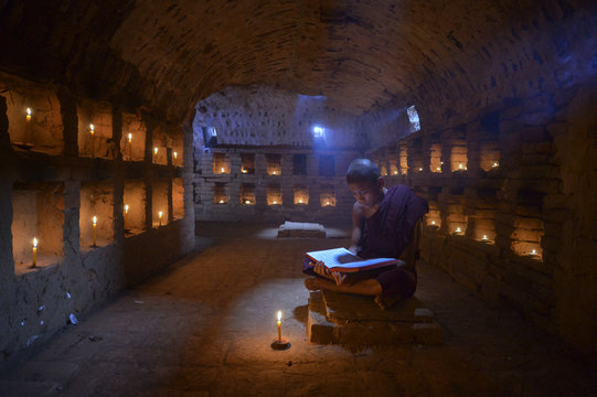 Monk reading book in candle light room