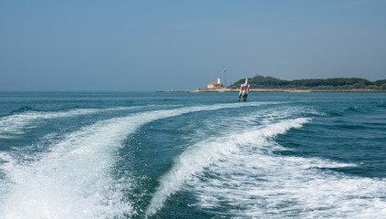 Bootswellen am Mittelmeer mit Leuchtturm im Hintergrund