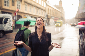 Woman stands under the rain screaming and enjoying.Portrait of young beautiful wet woman standing on the street with her hands spread enjoying rain falling on her.Refreshment enjoying life concept