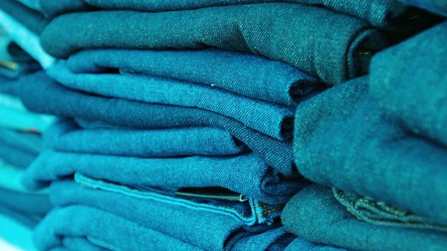 Video FullHD - Many pairs of denim blue trousers, folded and neatly stacked in a public market.