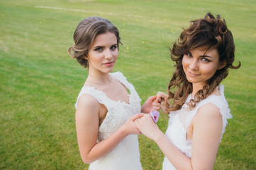 Two beautiful brides holding hands on the green field of the golf club