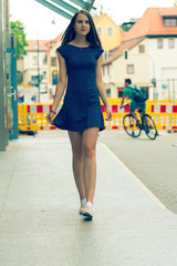 Pretty girl with long hair wearing a short dress and sneakers in the city. Toned photo