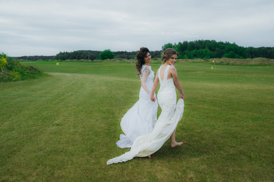 Two beautiful brides walking on the green field of the golf club