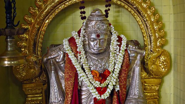 Video 1080p - Intricately detailed, metal sculpture of a Hindu god, with a ruby on its forehead and garlands of flowers around its neck, inside a temple.
