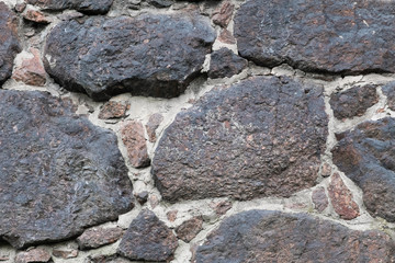 Wall of the medieval fortress of large stones. The texture is very old stone walls of the fortress. Background of cobblestones. The ancient construction of buildings from natural stones.