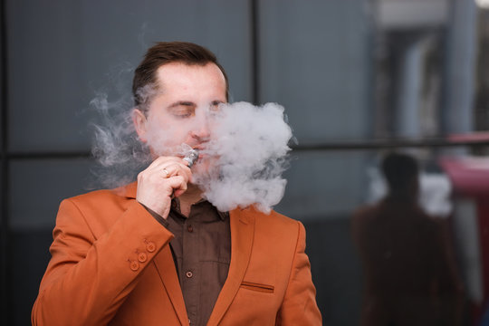 Young man smoking electronic cigarette on background of building