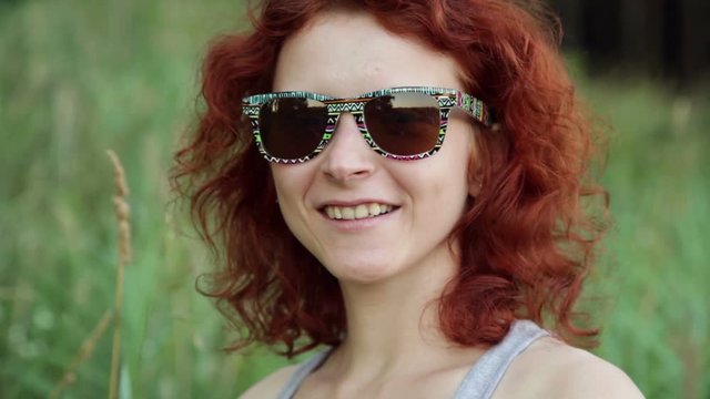 Close up ginger woman in sunglasses smiling against green grass