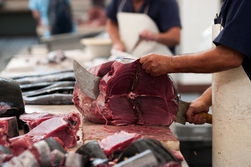 Fisherman (salesman) is cutting fresh tuna fish in the open air fish market or restaurant. Mercado...