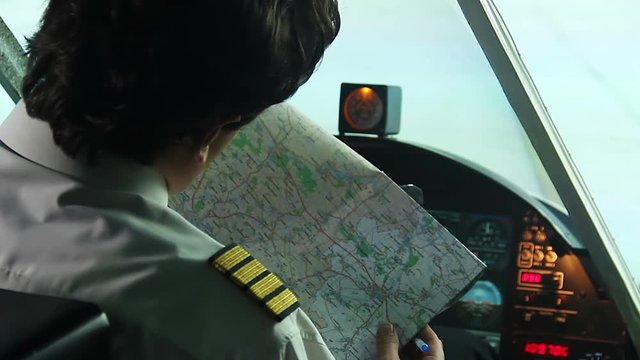Young male pilot sitting in cockpit, marking place of arrival on map, planning