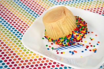 upside down cupcake with birthday candle and colorful sprinkle dots on white plate