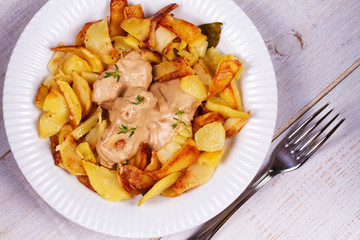 Fried potato with chicken breast and cream sauce in white plate. View from above