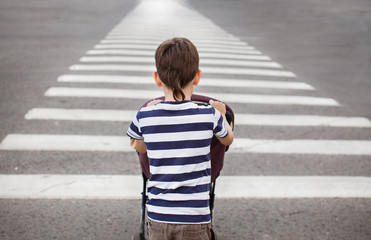 boy with the stroller on a pedestrian crossing. older brother carries the stroller with the baby...