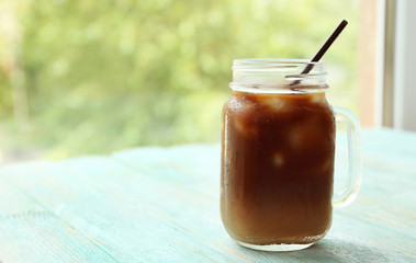 Glass jar of iced coffee on blurred natural background