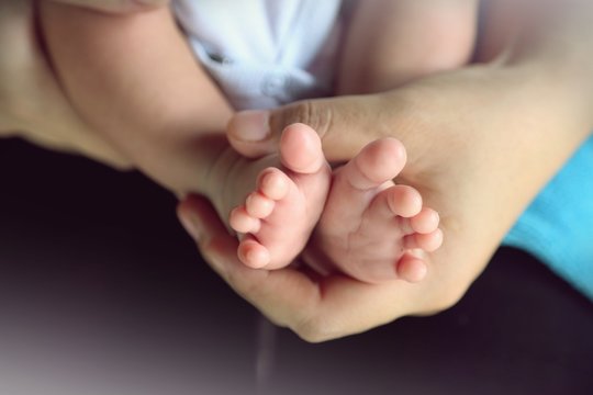 Photo of newborn baby feet and hand in soft focus