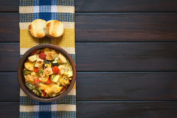 Herzhafter Brotpudding mit Gemüse (Zucchini, Paprika, Tomate) in rustikale Schüssel, fotografiert auf dunklem Holz mit natürlichem Licht 