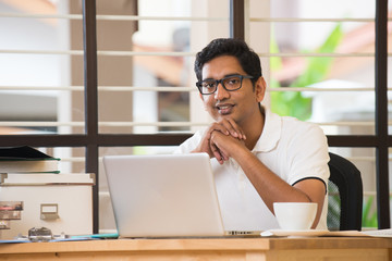 casual indian man smiling and working at office