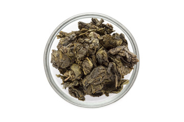 Organic Green Tea (Camellia sinensis) dried whole leaves in glass bowl isolated on white background. Macro close up. Top view.