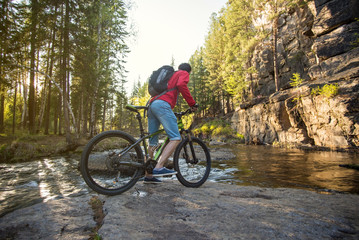 Naklejka premium Cyclist with a backpack traveling on a mountain river at sunset