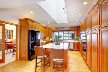 Brown wooden kitchen interior with black built-in fridge and white ceiling with skylight.