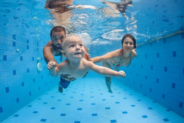 Happy full family - mother, father, baby son learn to swim, dive underwater with fun in pool to keep fit. Healthy lifestyle, active parent, people water sport activity, swimming lesson. Focus on child