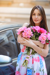 Woman with flowers peonies outdoors near the car