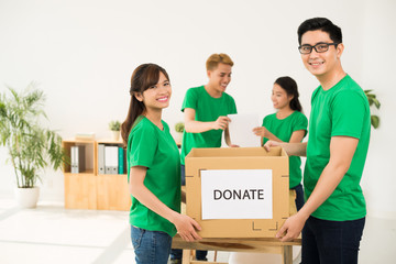 Young Asian volunteers holding cardboard box with donate inscription