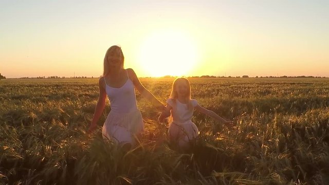 The young woman with the girl go to the field of wheat at sunset
