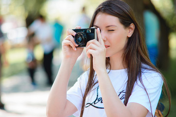 Young woman making photos with vintage film camera at park.