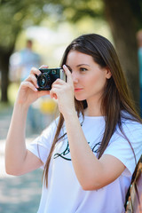 Young woman making photos with vintage film camera at summer green park.