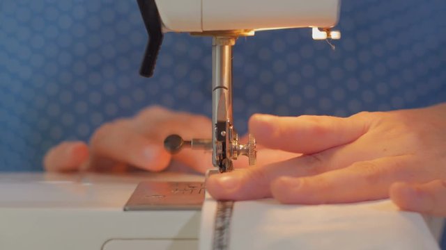 woman's hand moves white fabric, sewing machine makes a stitching