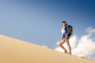 Young beautiful woman backpacker traveling in the desert. Sandy dunes and blue sky on sunny summer day. Travel, adventure, freedom concept. Toned.