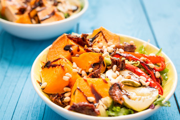 Healthy Paleo Salad with Pumpkin, Sweet Potato, Red Pepper and Nuts on Blue Wooden Background, Close-up