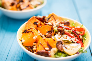 Healthy Paleo Salad with Pumpkin, Sweet Potato, Red Pepper and Nuts on Blue Wooden Background, Close-up